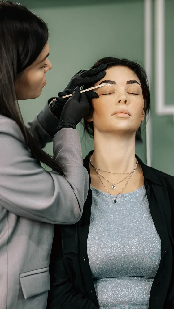 Esthéticienne appliquant la teinture sur les sourcils et les cils d'une cliente