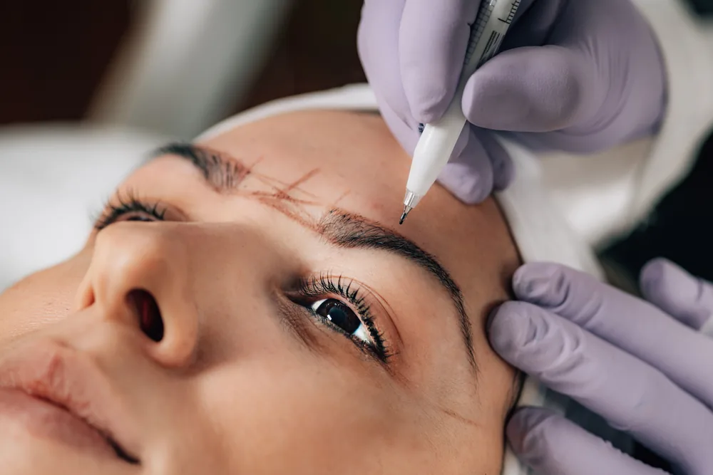 Esthéticienne traçant la forme des sourcils d'une cliente avant un brow lift