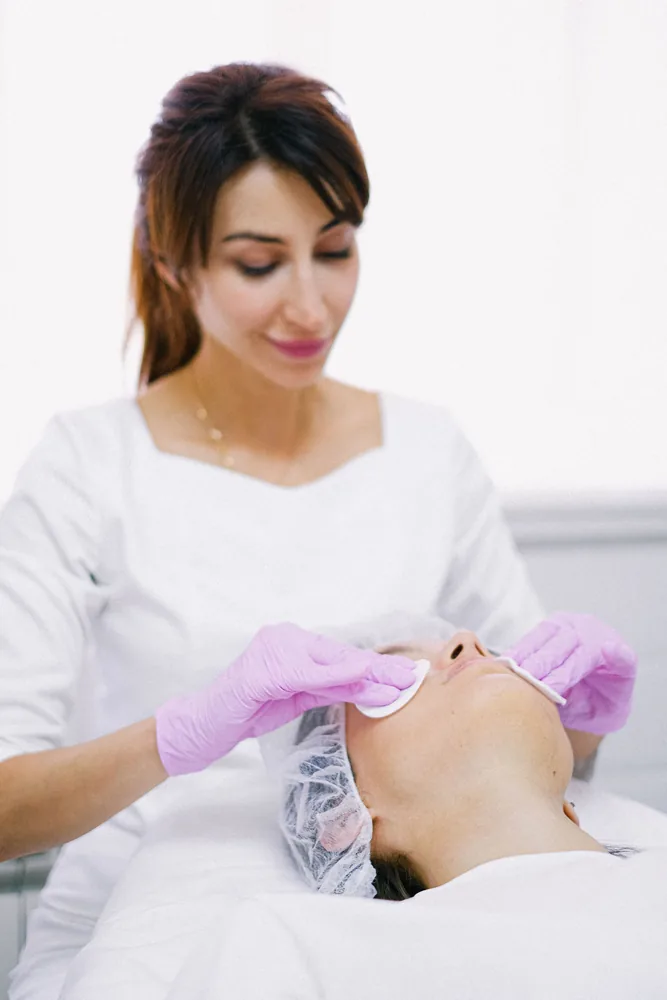 Esthéticienne démaquillant le visage d'une cliente allongée
